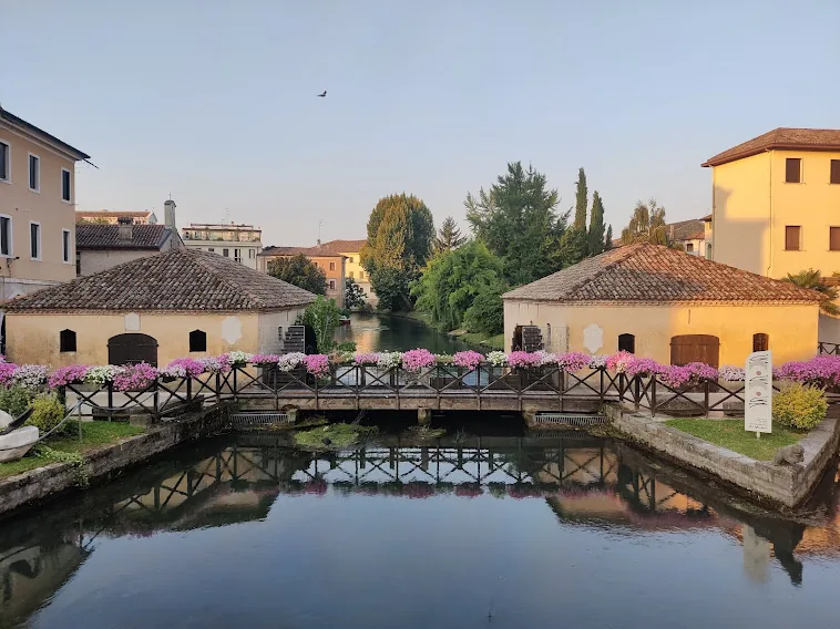 Gli antichi mulini di Portogruaro affacciati sul fiume Lemene con un ponte fiorito